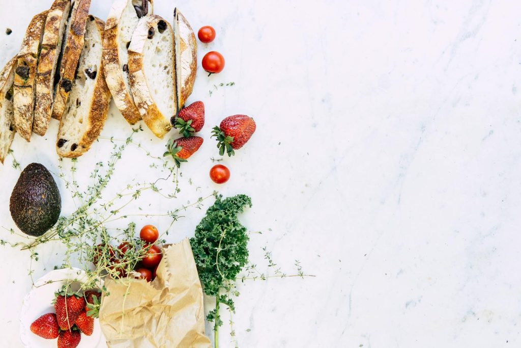 A flat lay of fresh ingredients including bread, strawberries, and avocado on marble. Perfect for food and lifestyle imagery.