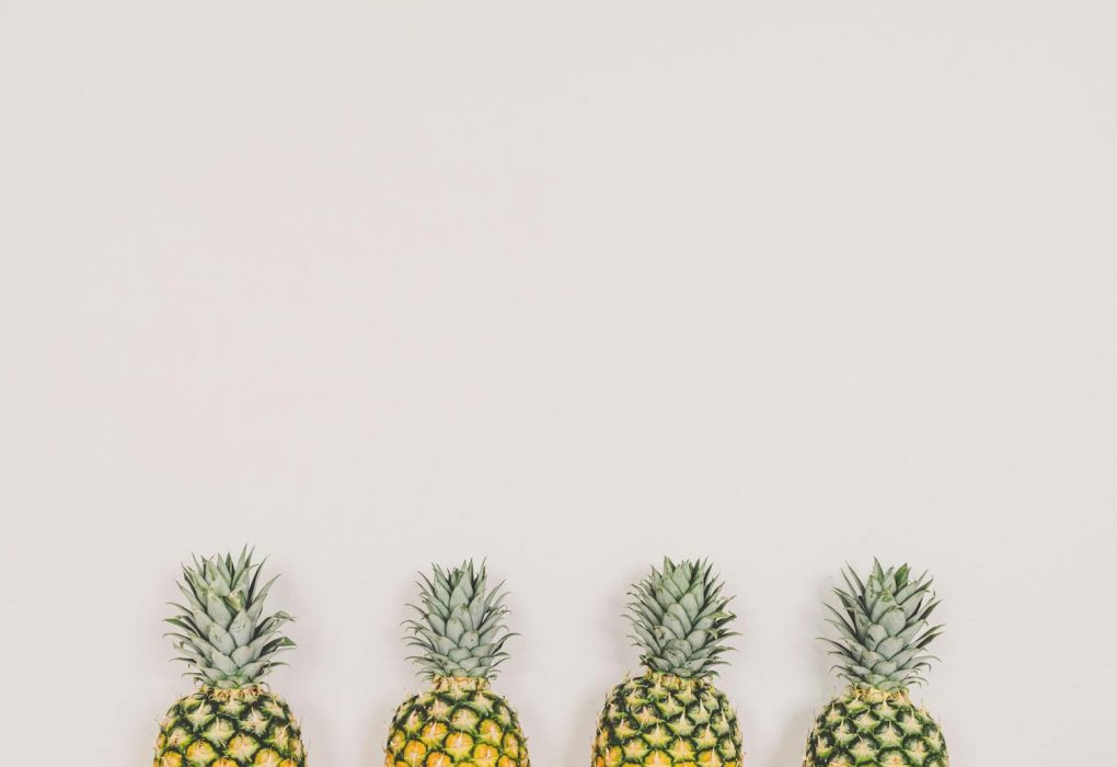 A minimalist image of four pineapples aligned on a white background, perfect for tropical themes.