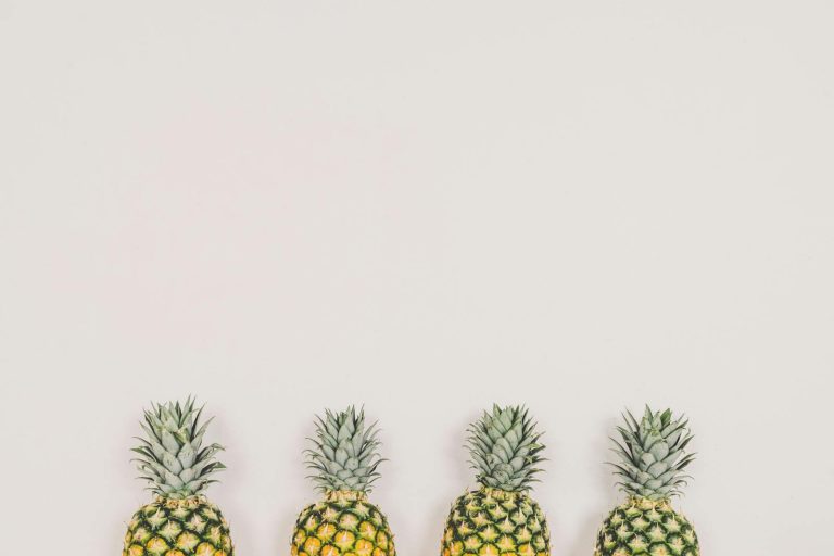 A minimalist image of four pineapples aligned on a white background, perfect for tropical themes.